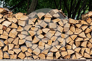 Woodpile from chopped birch firewood with bark and knots lies on green dark background