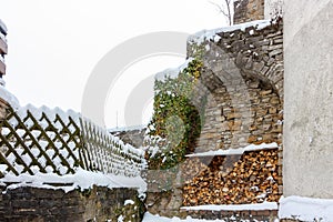 Woodpile with firewood and an old wooden fence covered with snowdrifts. Snow is a rare occurrence in the historic spa town of Bad