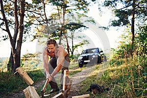 Woodsman with an axe cutting wood. Handsome shirtless man with muscular body type is in the forest at daytime