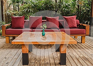 Woodwn table and sofa with red cushion on wooden floor in garden.