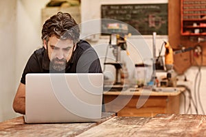 Woodwork designer with a beard in his workshop using laptop