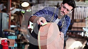 Woodworker in apron sanding the edge of guitar body using manual tool with sanding paper