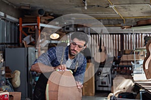 Woodworker in apron sanding the edge of guitar body using manual tool with sanding paper