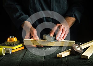 The woodworker cleans a wooden planks with an abrasive tools. Hands of the builder close-up during work. Renovation or