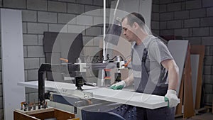 Woodworker is drilling holes in particle board in workshop, using industrial drill machine, furniture assembling