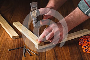 Woodworker hammers a nail into a plank with a hammer. Hands of the master close-up. Working environment in a carpentry workshop