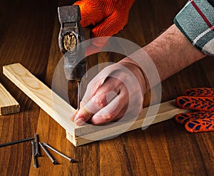 Woodworker hammers a nail into a plank with a hammer. Hands of the master close-up. Working environment in a carpentry workshop