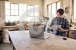 Woodworker reading notes and using a laptop in his workshop