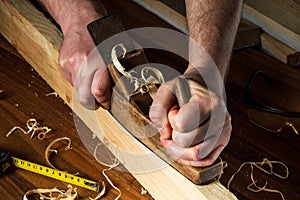 Woodworker using a hand plane to clean up a wooden board. Hands of the master closeup at work. Working environment in a carpentry