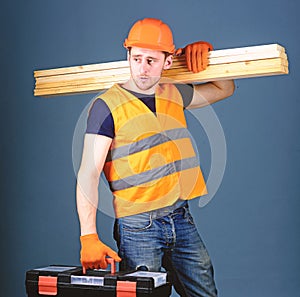 Woodworking concept. Carpenter, woodworker, labourer, builder on calm face carries wooden beams on shoulder. Man in