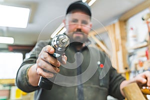 Woodworking tools concept. Adult man pointing at camera with electric drilling machine. Blurred male carpenter