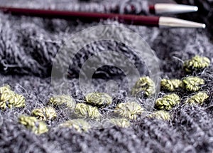 Wool sweater in the process of being knitted. Photo shows textured knitting including stripes, bobbles, knitting needles, yarn.