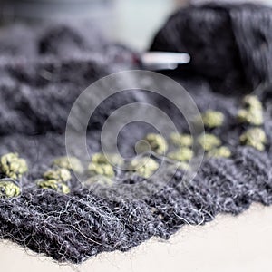 Wool sweater in the process of being knitted. Photo shows textured knitting including stripes, bobbles, knitting needles, yarn.