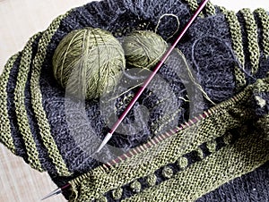 Wool sweater in the process of being knitted. Photo shows textured knitting including stripes, bobbles, knitting needles, yarn.