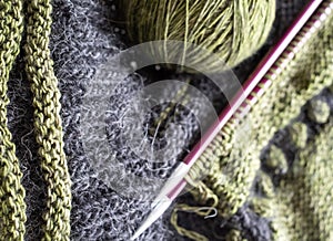 Wool sweater in the process of being knitted. Photo shows textured knitting including stripes, bobbles, knitting needles, yarn.