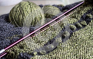 Wool sweater in the process of being knitted. Photo shows textured knitting including stripes, bobbles, knitting needles, yarn.