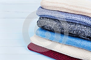 Wool sweaters and knitted winter clothes on blue wooden background. Copy space for text.