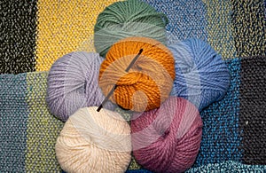 Wool yarn balls of various colors with crochet needle, thick wool for knitting and crochet against knitted background