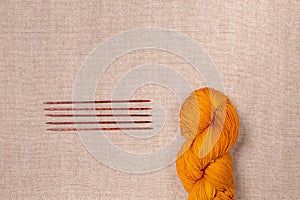 Wool yarn of orange color with wooden knitting needles
