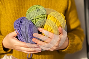 Wool yarn in yellow, purple and green. Knitting hobby.Skeins of yarn of various colors in hands in a in a mustard wool