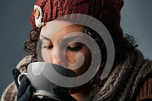 Woolen-clad woman savors latte, vivid eyes shining