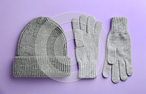 Woolen gloves and hat on violet background, flat lay