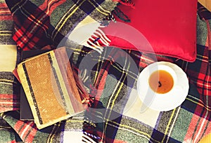 Woolen plaid, cup of tea, old books, red pillow on wooden background. Top view. Toned