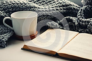 Woolen scarf, a cup of tea and book on the windowsill. Hygge and cozy autumn concept