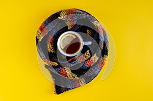 Woolen scarf with tea cup and lemon slice composition on yellow background