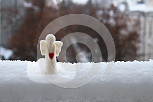 A woolen toy angel stands in the snow on the railing of the balcony against the street. Cloudy winter day