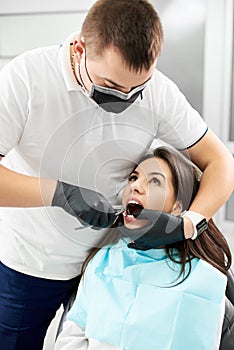 Wooman in dental chair, dentist pinches her tooth with forceps