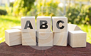 The word ABC is made up of wooden cubes lying on an old tree stump against a blurred garden background.