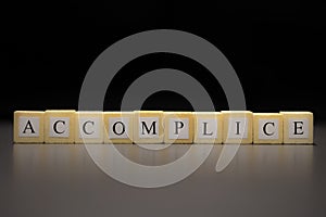 The word ACCOMPLICE written on wooden cubes, isolated on a black background photo