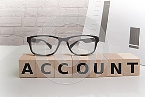 The word ACCOUNT ON WOODEN cubes on a light office background with glasses and papers, business concept