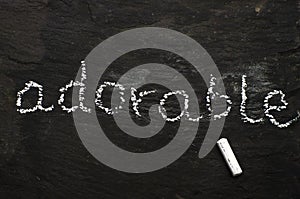 The word adorable written with chalk on black stone.