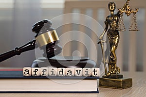Word AFFIDAVIT composed of wooden dices. Wooden gavel and statue of Themis in the background