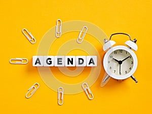 The word agenda on cubes with alarm clock and paper clips. Business agenda, event and schedule planning