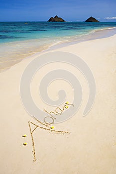 The word aloha is written on sand