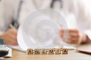 Word anemia on table and blurred doctor filling out medical paperwork in background.