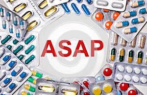 The word ASAP is written on a light background surrounded by multi-colored packages with pills. Medical concept