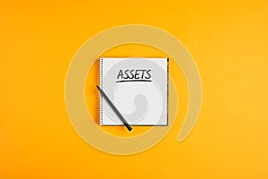 The word assets written on notebook with pen on yellow background with copy space. Inventory asset management