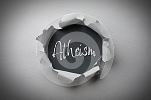 Word Atheism on black background, view through hole in grey paper