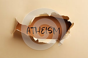 Word Atheism on brown background, view through hole in beige paper