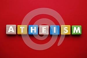 Word Atheism made of wooden cubes with letters on red table, top view