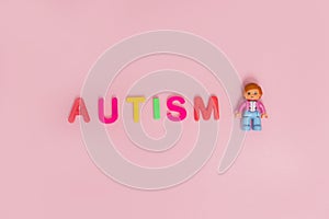 Word AUTISM and toy on pink background, top view