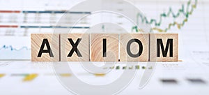 Word AXIOM made with wood building blocks on background from financial graphs and charts