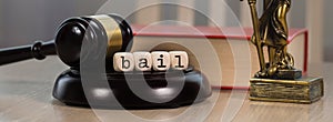 Word BAIL composed of wooden dices. Wooden gavel and statue of Themis in the background