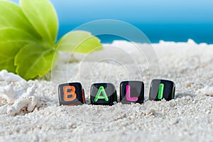 Word Bali is made of multicolored letters on snow-white sand against the blue sea.