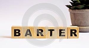 The word BARTER on wooden cubes on a light background near a flower in a pot. Defocus