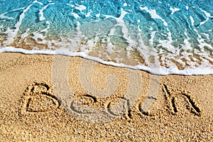 Word BEACH written on yellow sand, blue sea wave, white foam top view close up, handwriting letters text, summer vacation, holiday